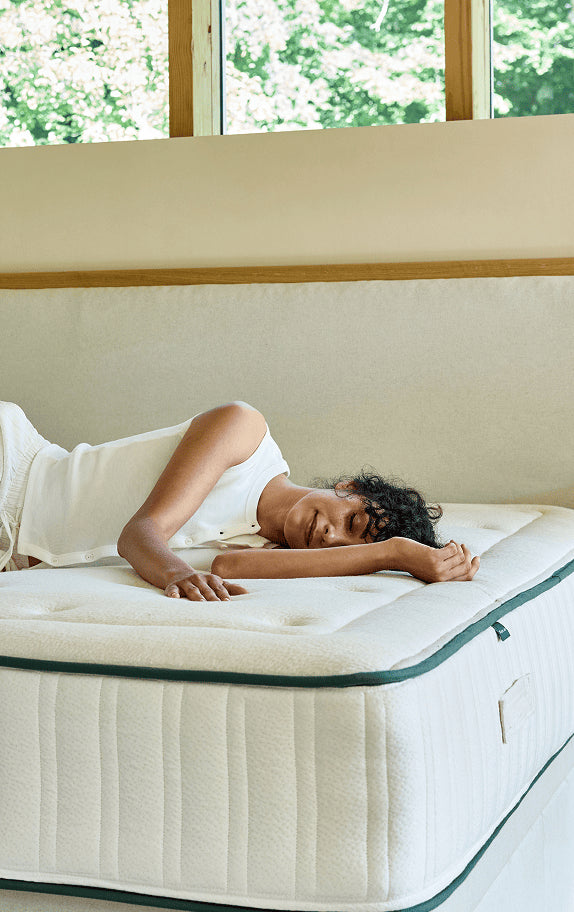 Femme allongée sur un matelas en latex naturel Kipli dans une chambre lumineuse, illustrant le confort et le maintien du matelas écoresponsable.