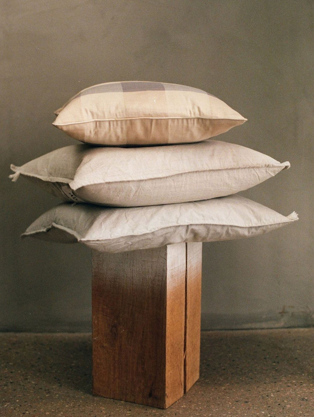 Coussins en tissu naturel empilés sur un support en bois brut, illustrant une décoration minimaliste et durable pour une chambre écologique.
